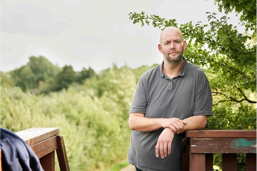 Mand der står ved et rækværk i naturen, brugt som neutral illustration i en informationssektion om svær overvægt hos voksne.
